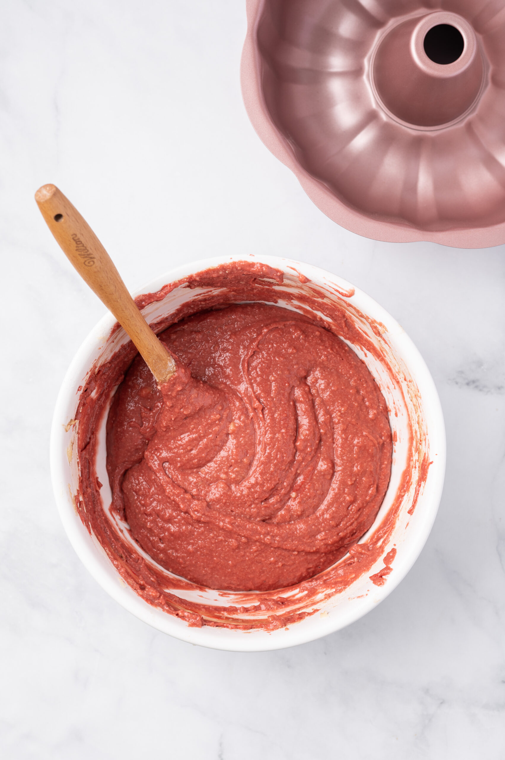 red velvet cake mix in a white mixing bowl with a rubber spatula sticking out of the bowl