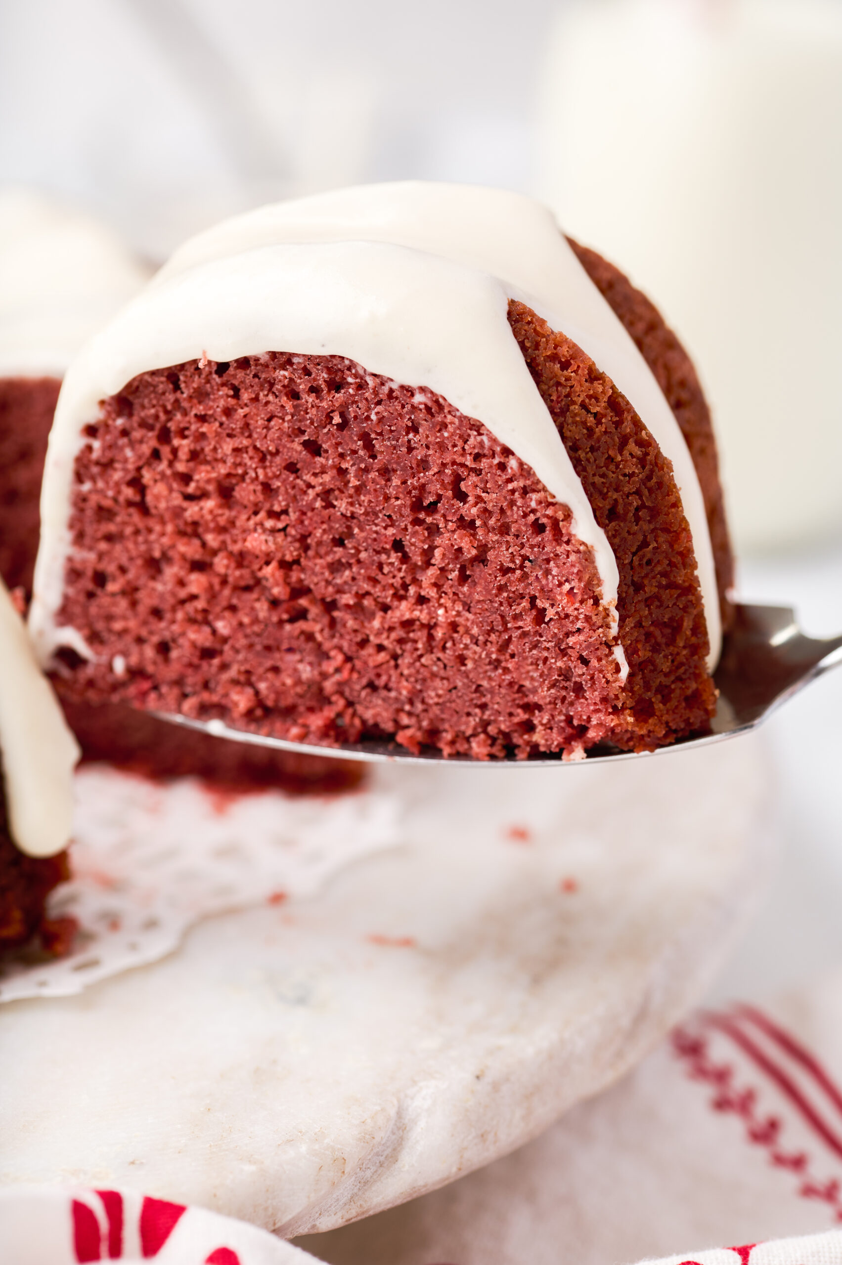slice of red velvet bundt cake frosted with cream cheese frosting held in the air on a cake server