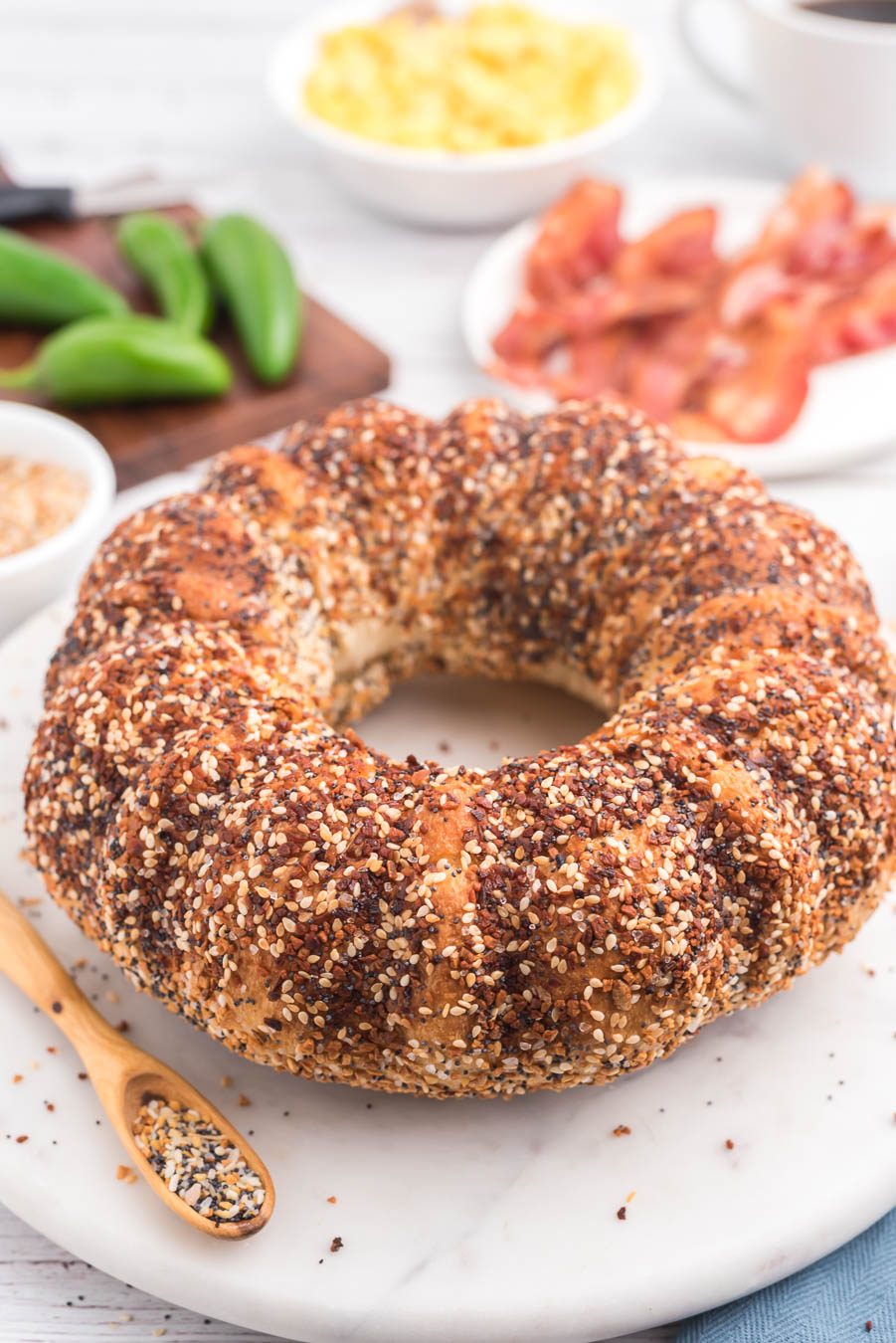 finished jumbo everything bagel on a marble cutting board with a wooden spoon next to it