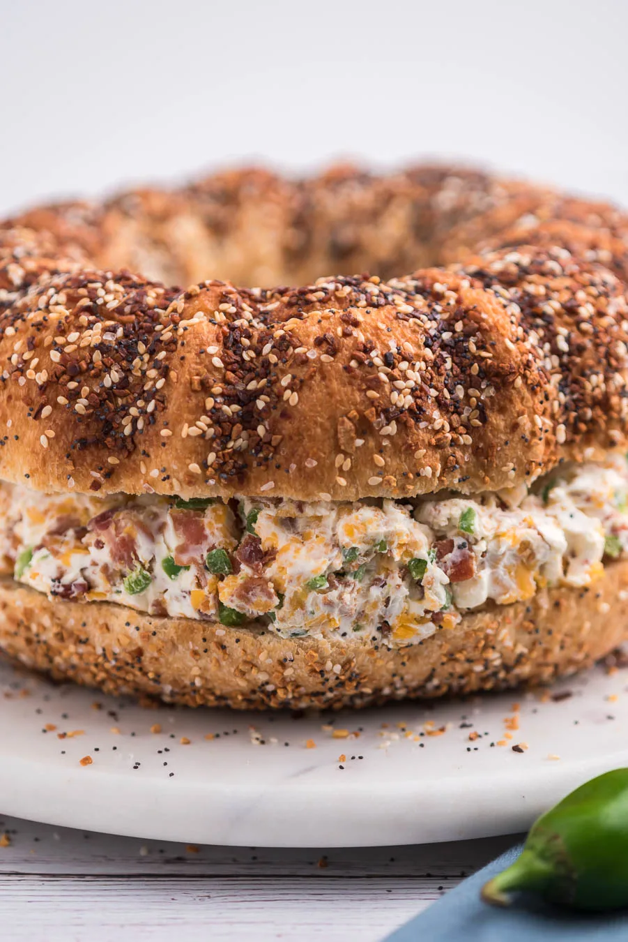 side view image of a jumbo everything bagel filled with jalapeno cream cheese with bacon