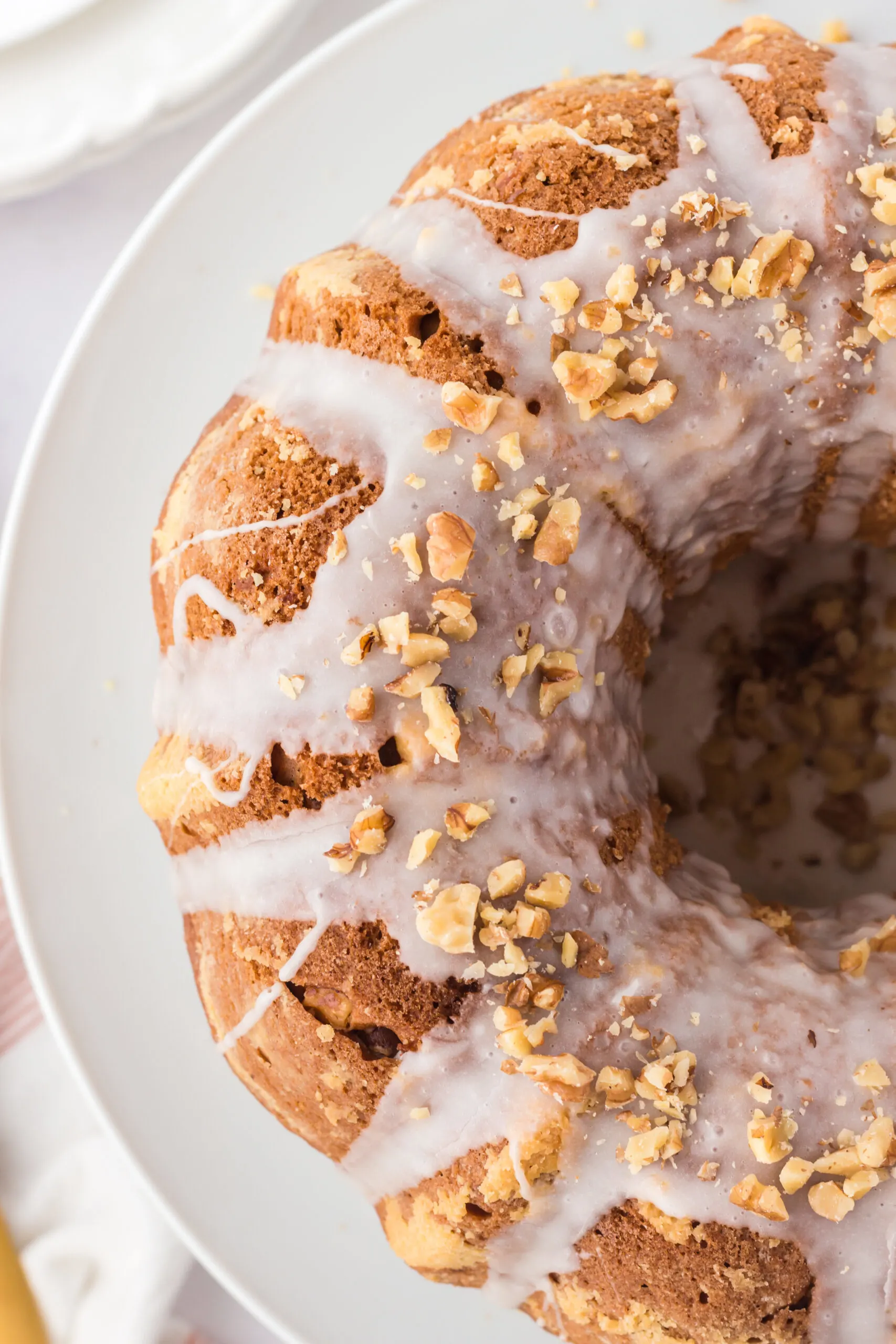 birds eye image of half of a maple walnut bundt cake on a white plate topped with chopped walnuts