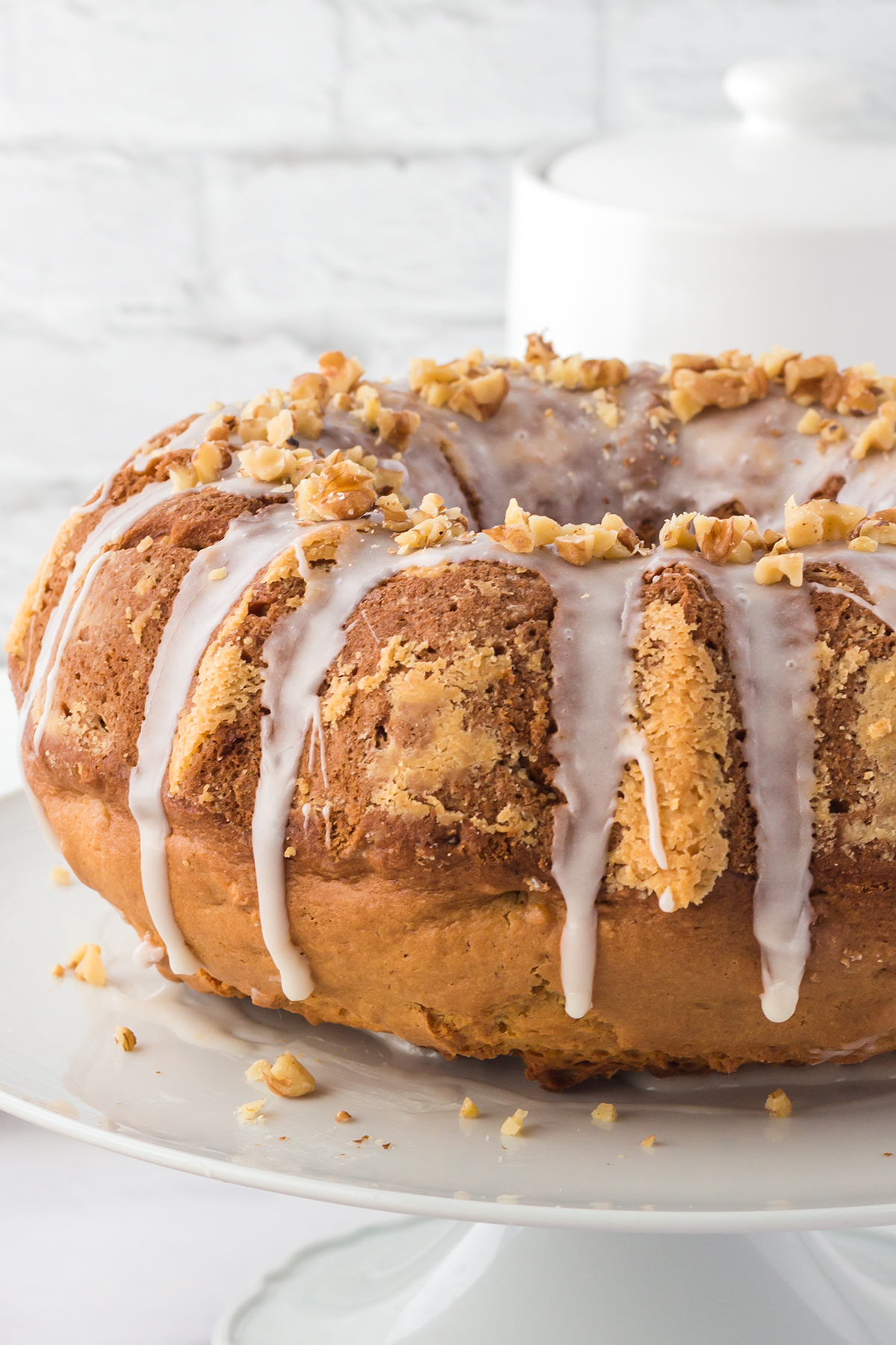off center side view image of maple walnut bundt cake on a white cake stand